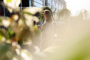 Woman in Gray Coat Standing Near Green Plants Woman in Gray Coat Standing Near Green Plants