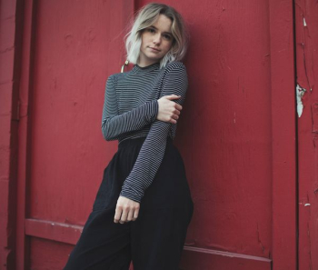 woman in gray top leaning her back on red wall