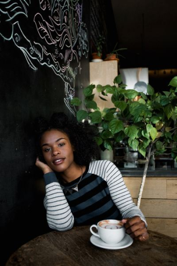 woman in white, black, and blue striped long-sleeved shirt sitting on chair in front of table holding white ceramic teacup