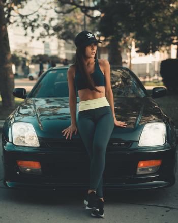 Woman Leaning On Black Car Wearing Black Cap And Sport Bra Woman Leaning On Black Car Wearing Black Cap And Sport Bra