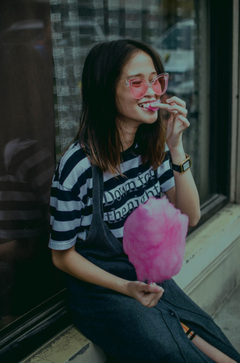 Woman Sitting Near Glass Wall Holding Cotton Candy Woman Sitting Near Glass Wall Holding Cotton Candy
