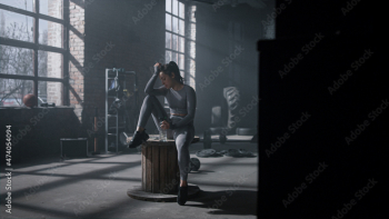 Woman sitting on wooden box in gym. Sportswoman holding sports bottle in hand