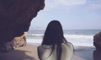 woman sitting under rock facing sea woman sitting under rock facing sea