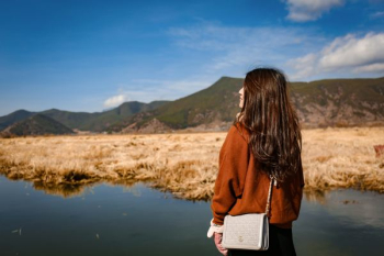 woman standing in front of green mountain under blue sky woman standing in front of green mountain under blue sky