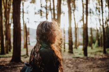 woman standing in middle of trees looking right