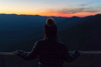 woman standing on roof while holding on fence looking on mountains