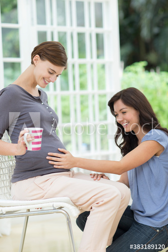 Woman touching stomach of pregnant friend Woman touching stomach of pregnant friend