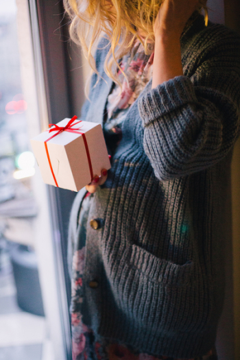 Woman Wearing Blue Knit Cardigan Holding Gift Box Inside Room