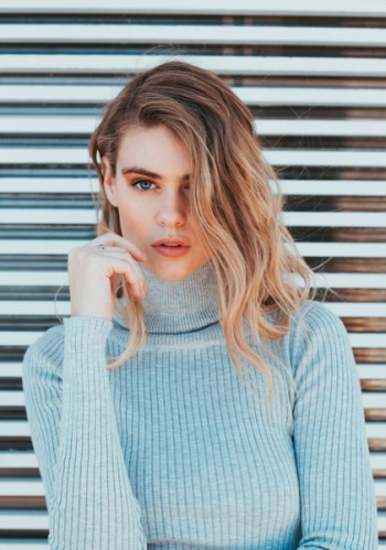 woman wearing gray turtle-neck top standing near white wall woman wearing gray turtle-neck top standing near white wall