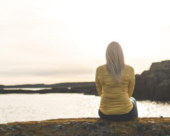 Woman Wearing Yellow Bubble Jacket Sitting in Front of Sea