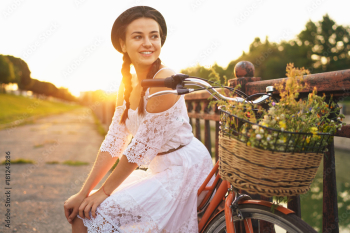 Young beautiful woman sitting on her bicycle with flowers at sunset