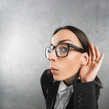 Young businesswoman listening with her hand on an ear against gray background