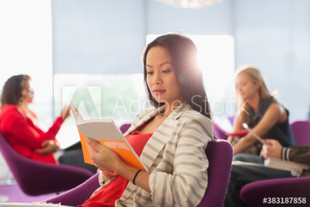 Young female college student reading book in student lounge Young female college student reading book in student lounge