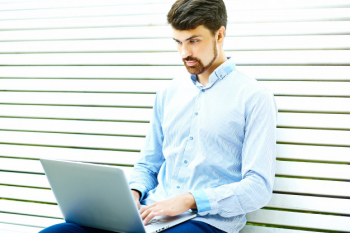 Young handsome smiling businessman model sitting on the park bench using laptop in casual hipster cloth Free Photo