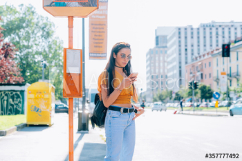 Young woman using smartphone while waiting at bus stop Young woman using smartphone while waiting at bus stop