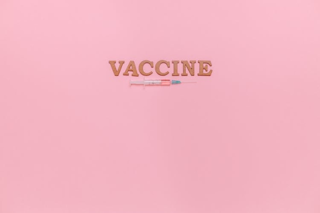 A Syringe and Vaccine Text on Pink Background