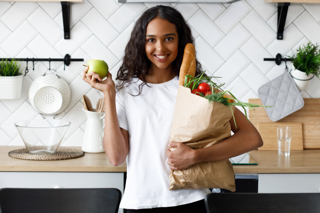 African girl stands on the kitchen and holds a paper bag with groceries Free Photo