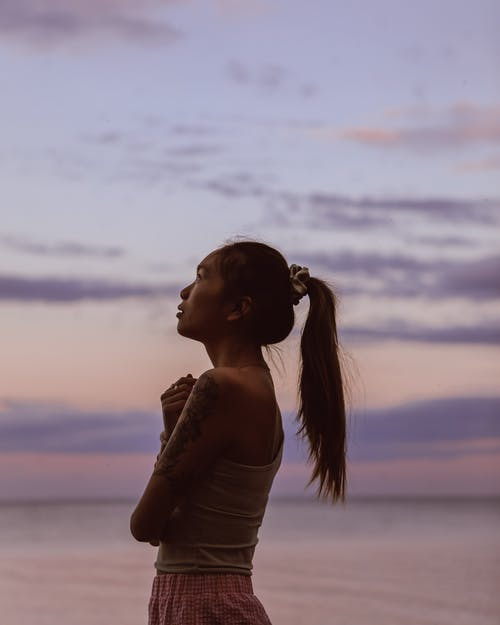 Asian woman standing on seashore at sunset · Free Stock Photo