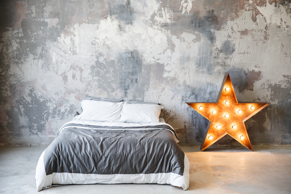 Bedroom in loft style and gray colors. Metal star with lamps and a bed near gray plaster wall