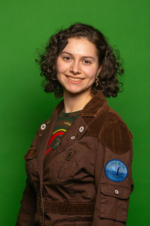 Cheerful Young Woman in Casual Brown Jacket with Green Background
