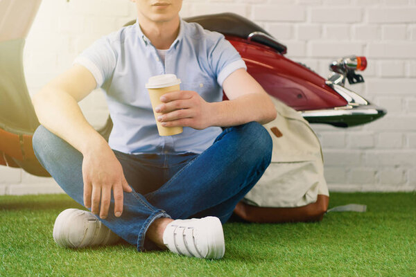 Cropped shot of young man with cup of coffee to fo sitting in front of vintage scooter