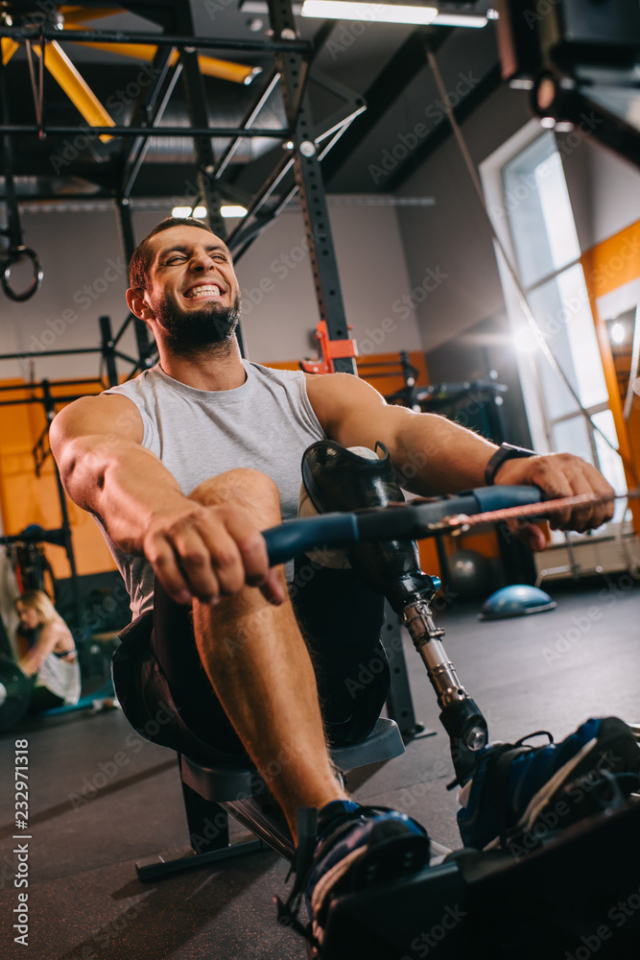 hardworking young sportsman with artificial leg working out with rowing machine at gym
