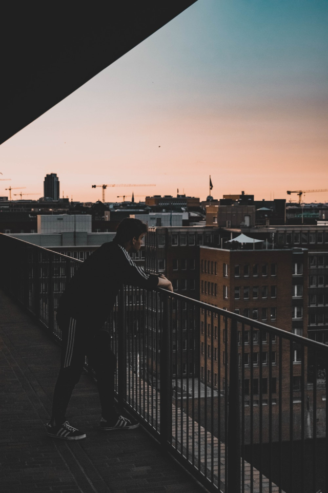 Photo of Man in Black and White Tracksuit Leaning on Balcony Railings