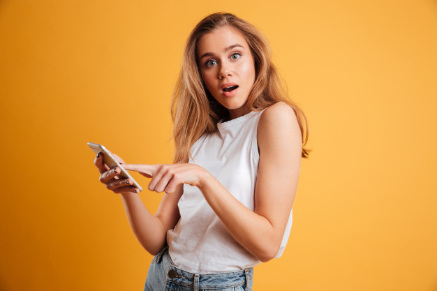 Portrait of a confused young girl holding mobile phone Free Photo