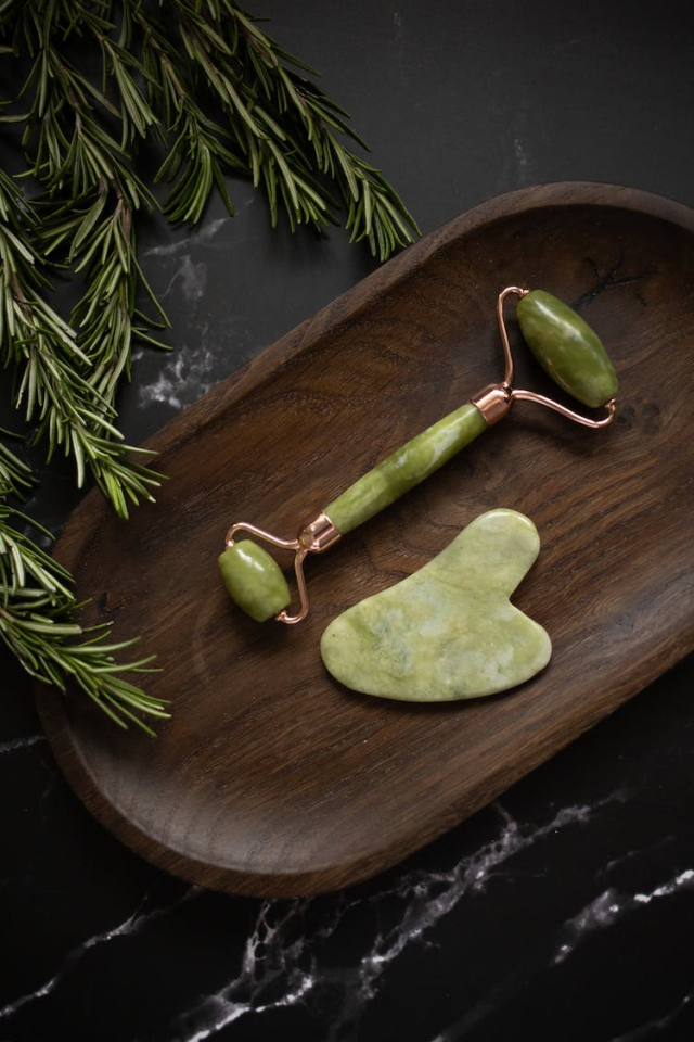 Set of facial massage tools placed on wooden plate on black table
