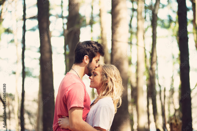 Side view of man kissing woman on forehead in forest