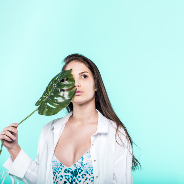 Woman in shirt and swimsuit standing and holding monstera leaf in hand Free Photo