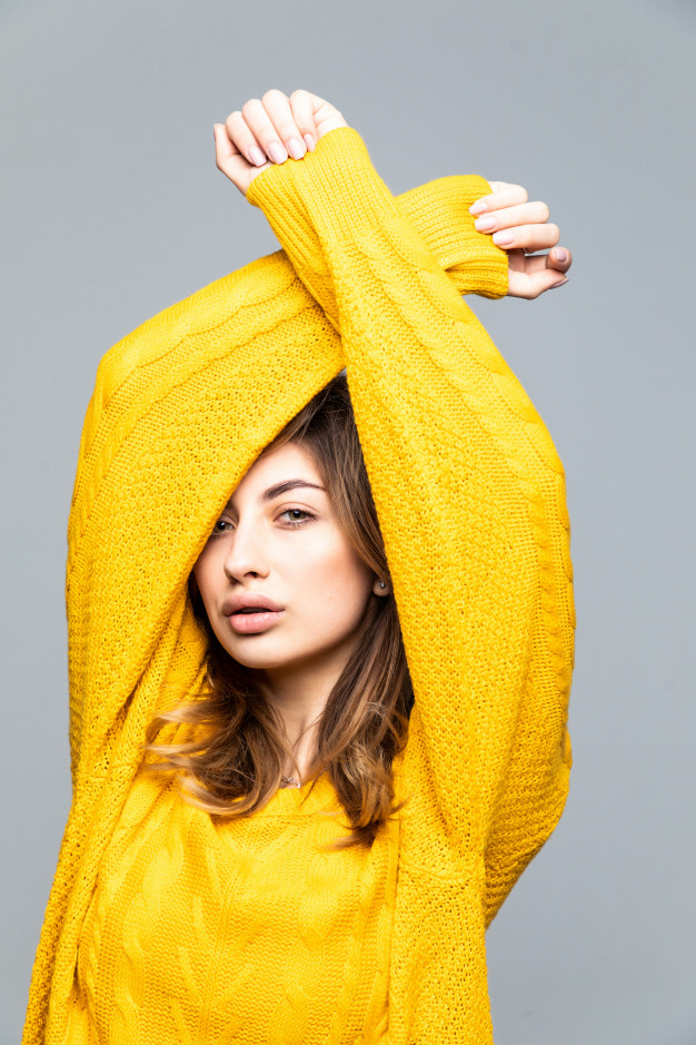 Young pretty woman in yellow sweater with raised hands isolated on gray wall Free Photo