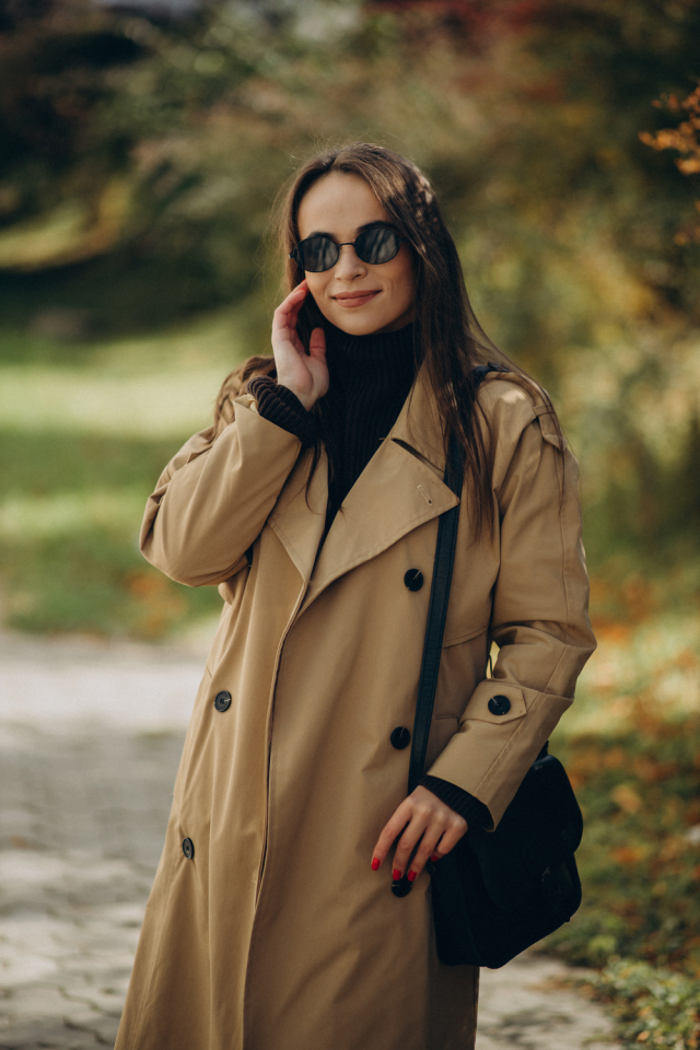 Young woman wearing trench-coat and sunglasses, posing in the city